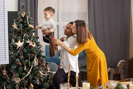 快乐的年轻家庭向儿子展示一棵圣诞树 配有木玩具和生态风格的装饰品图片