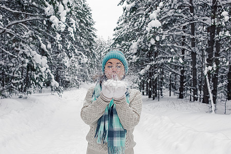 一个女孩站在冬天的森林里 手里拿着雪 吹着它图片
