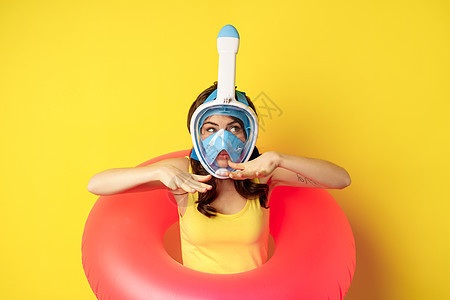 穿着潜水面具的漂亮女孩 正在打呼哨 戴着游泳环 展示游泳运动 在黄色背景上站立图片