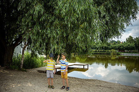 兄弟姐妹 兄弟 拥抱 两个孩子 大男孩和他的弟弟站在老树附近的湖岸上 夏季假期概念休闲时间在大自然中 生活 太阳镜图片