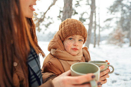 年轻女子和儿子在冬季森林野餐喝热茶 家庭图片