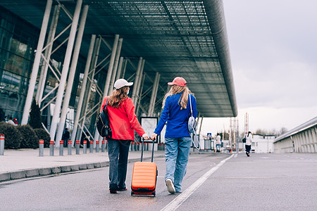 两个快乐的女孩在机场附近行走 带行李 空中旅行 暑假 女孩们 手提包图片