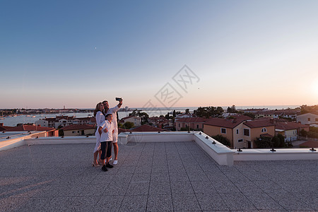 快乐的家庭在日落时在家里屋顶上拍自拍和智能手机 有选择的焦点 团体 反射图片