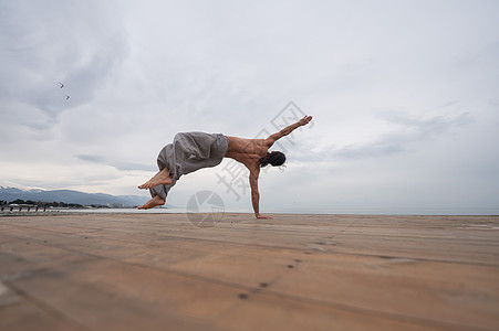 不穿衣服的caucasian男人在小石头沙滩上做背翻 自由 跑酷图片