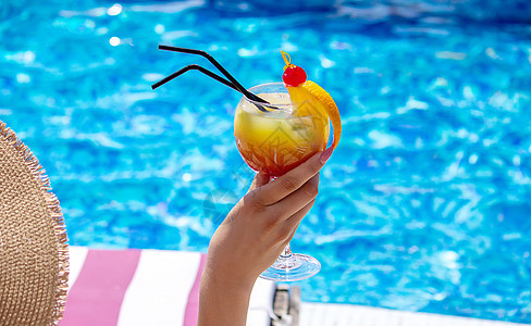 在泳池附近的一个护晒员上的女孩 喝着一杯新鲜的橙子鸡尾酒 太阳帽 异国情调图片