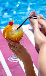 在泳池附近的一个护晒员上的女孩 喝着一杯新鲜的橙子鸡尾酒 放松 夏天图片