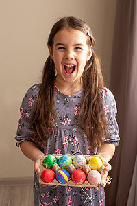 一个有趣的黑发女孩 穿着衣服 拿着一个装满彩色鸡蛋的纸板盘图片