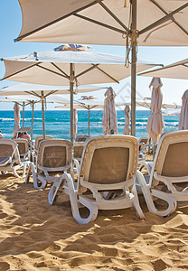夏季在金沙滩上用树荫保护伞遮盖的防晒阳光下铺有整排塑料坐椅/休息室躺椅/休息室图片
