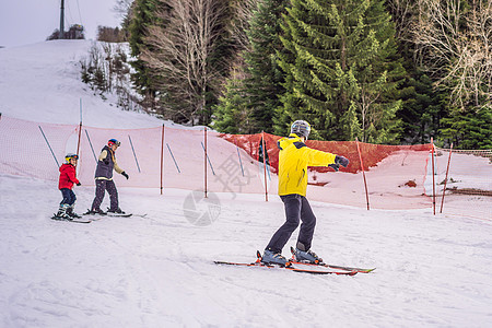 妈妈和儿子正在跟着教练学习滑雪 带安全帽 护目镜和杆的活跃蹒跚学步的孩子 幼儿滑雪比赛 家庭的冬季运动 高山学校的孩子们滑雪课 图片