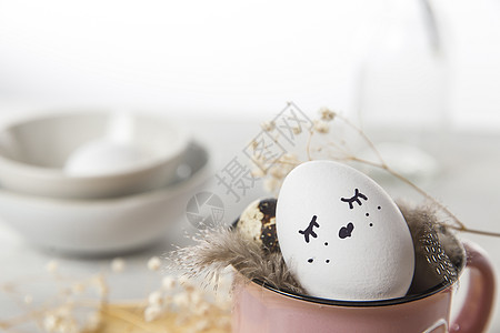 复活节概念 一个白蛋 有铜丝耳朵和在杯子上涂漆的兔子睡脸 帕崔奇鸡蛋和羽毛 装饰风格 填料图片