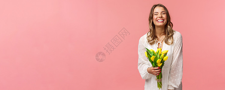 假期 美丽和春天的概念 无忧无虑 快乐 迷人的金发女孩 身穿白色裙子 手捧黄色郁金香 笑得开心 站在粉色背景下 有浪漫的约会 女图片