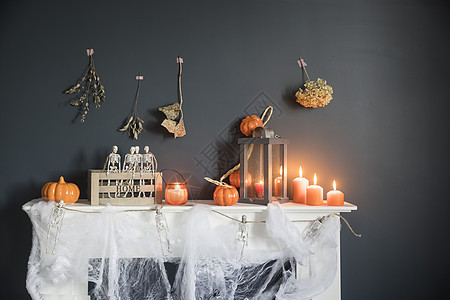 万圣节家居装饰 深蓝色墙壁壁炉旁木箱中的塑料玩具骨架 骷髅花环 梳妆台上的蜘蛛网 橙色蜡烛和灯笼 绳索 盒子图片