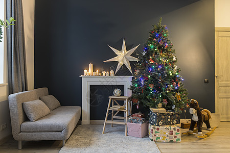圣诞节前的家居装饰 装饰有花环灯的圣诞树 摇马 用精美纸包裹的礼物 带有大白纸星星和蜡烛的人造壁炉 沙发 地毯图片