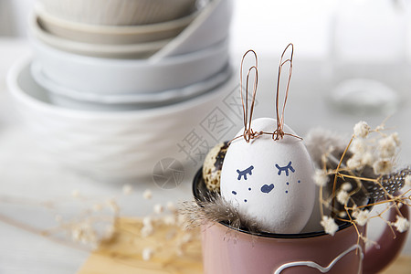 复活节概念 一个白蛋 有铜丝耳朵和在杯子上涂漆的兔子睡脸 帕崔奇鸡蛋和羽毛 野兔 盘子图片