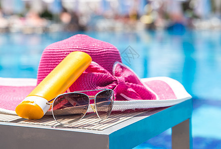 在酒店游泳池旁边的 一瓶太阳霜 帽子和墨镜 美丽的 水图片