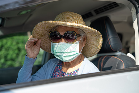 身戴面具和帽子的亚洲老年妇女坐在车里 在旅行中享有享受和自由图片