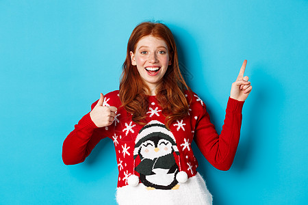 圣诞快乐 穿着Xmas毛衣的红头红发女孩 指向右上角 展示新年的宣战和举起掌声 雀斑 快乐的图片