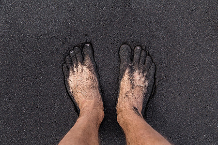 一个人赤脚站在特纳里费海滩的火山黑沙滩上 两英尺高在沙面上图片