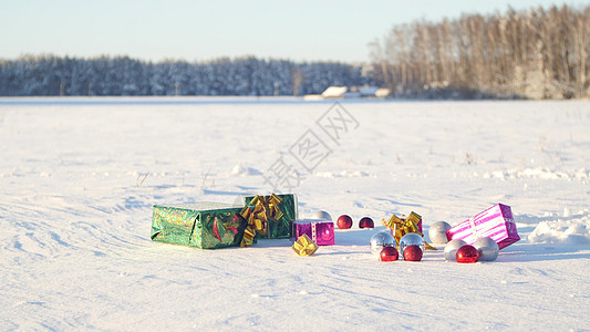 在阳光明媚 寒冷和晴朗的户外天气下 雪地上放着圣诞礼物 嘉年华 球图片