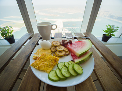 在迪拜棕榈树上的摩天大楼窗户背景上 配有炒蛋和水果的轻便早餐图片