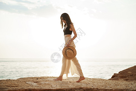 年轻时尚的女人 日落时站在海边悬崖上 水图片