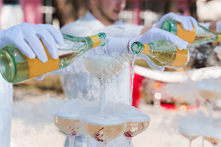 侍应员将香槟从两瓶倒入晶杯中 里面有干冰和白烟 紧贴在一起 葡萄酒在红酒杯中灌注图片