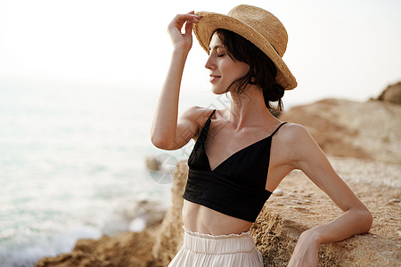 身穿黑胸围和白裤子的女子肖像 在海滩上靠在岩石上图片