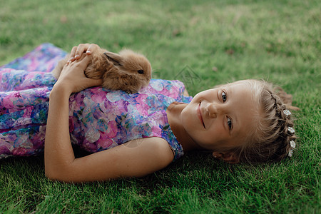 小姑娘和兔子坐在绿草地上 复活节那天 可爱的小女孩拿着兔子在她手里 夏天 幸福图片