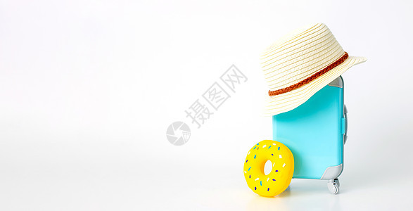 车轮上的蓝色手提箱 草帽和白色背景的黄色充气甜甜圈摊 轮子 包图片