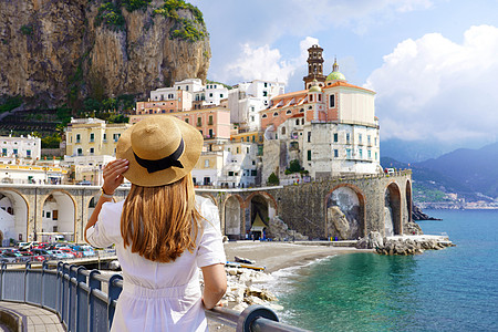 在意大利度假 身穿白色连衣裙 头戴帽子的年轻女子的背影 望着意大利阿马尔菲海岸的阿特拉尼村图片