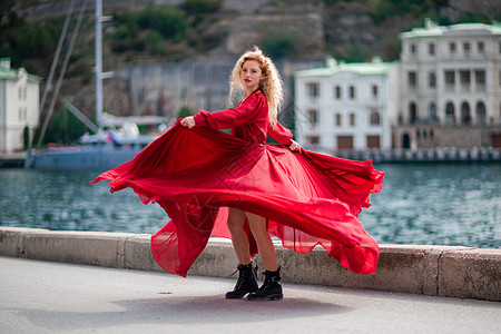 身着红裙的女子 长着丝绸长翅膀的时装模特 身着飘逸的裙子 在堤岸上飞舞着布料 步行 艺术图片