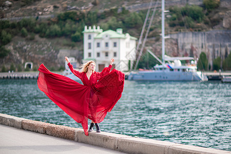 身着红裙的女子 长着丝绸长翅膀的时装模特 身着飘逸的裙子 在堤岸上飞舞着布料 美丽 时尚图片
