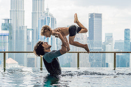 父亲和儿子在户外游泳池里 蓝天有城市风景图片