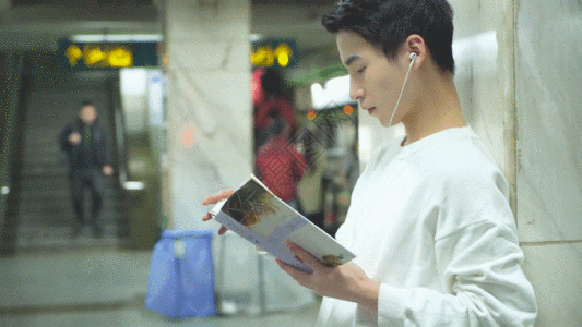 耳机学习男青年在地铁站着看书GIF高清图片