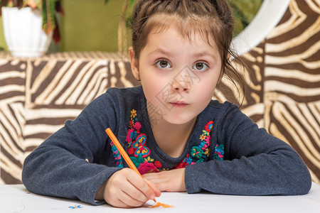 美丽的小女孩画铅笔坐在桌子上用眼睛睁大的眼睛看镜头图片