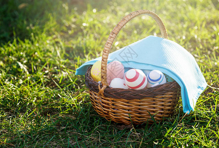 用蓝色毛巾在绿草上的藤篮中手绘复活节彩蛋在阳光明媚的春日复活节的传图片