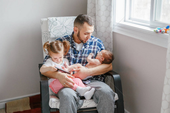白人父亲和蹒跚学步的女儿和刚出生的婴儿子坐在智能手机上看卡通片坦率真实的生活方式家庭生活单亲图片