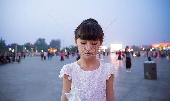 傍晚小女孩穿着白裙站在广场上闭着眼睛图片