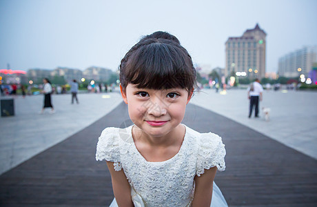 傍晚小姑娘穿着白裙站在广场上露出特殊的表情背景图片