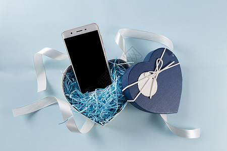 情人节爱心礼盒缎带手机在浅蓝色背景上图片
