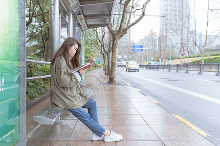 街景特写公交亭边等车边看书的女生背景