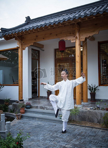 一位道士在古老的房屋前练习武术图片