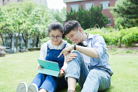 清新草地阳光下男女大学生在看平板电脑背景