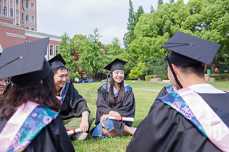 穿学士服毕业大学生坐草地聊天图片