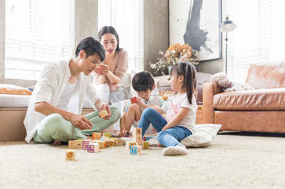 年轻父母陪孩子在客厅搭积木图片