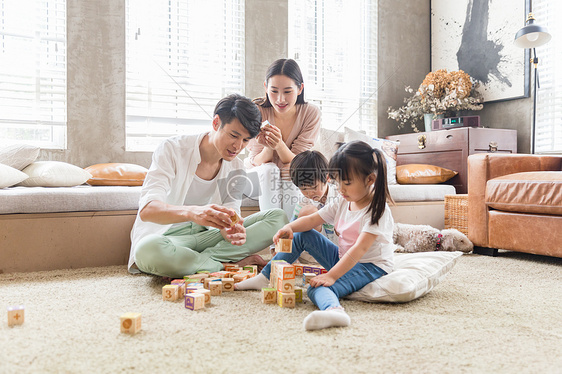 年轻父母陪孩子在客厅搭积木图片