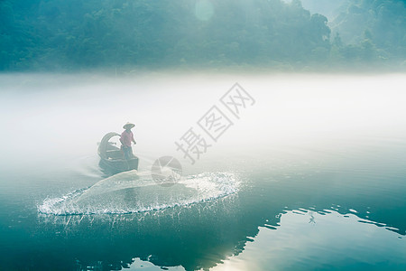 渔夫在起雾的江中撒网打鱼图片