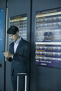商务男士在机场时刻表前拿手机观察背景图片