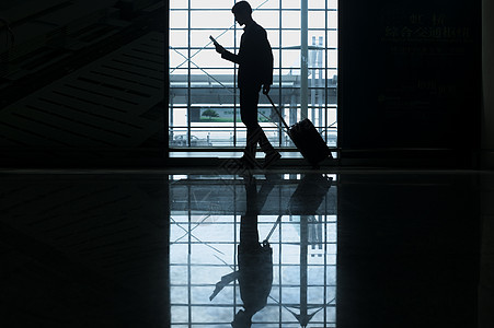 出差出发到达机场商务男士手提拉杆箱经过机场一边看着手机背景
