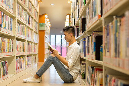 坐在图书馆书架旁看书的男生图片